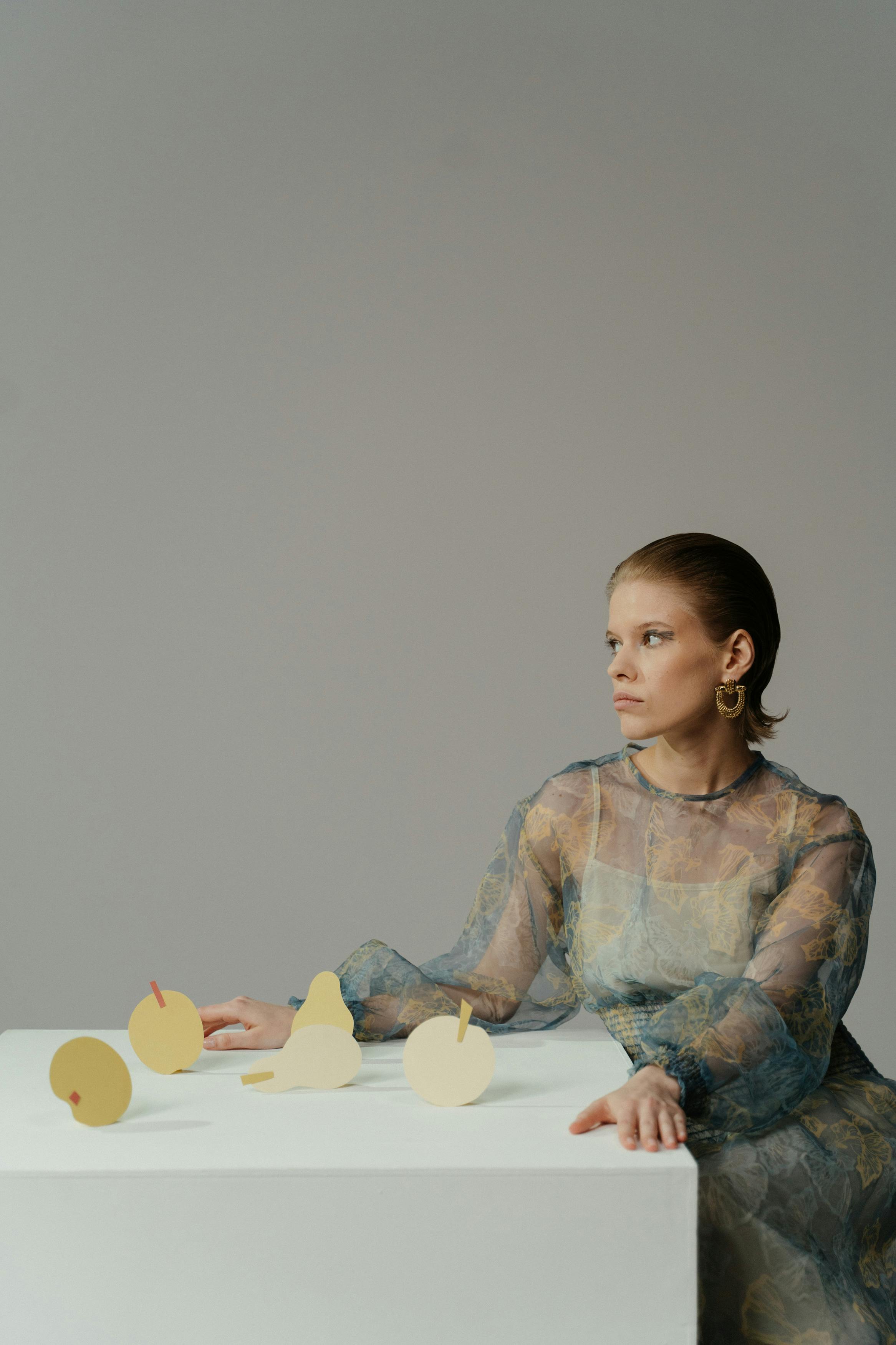 Caucasian woman in conceptual style sitting with paper cutouts at a table.