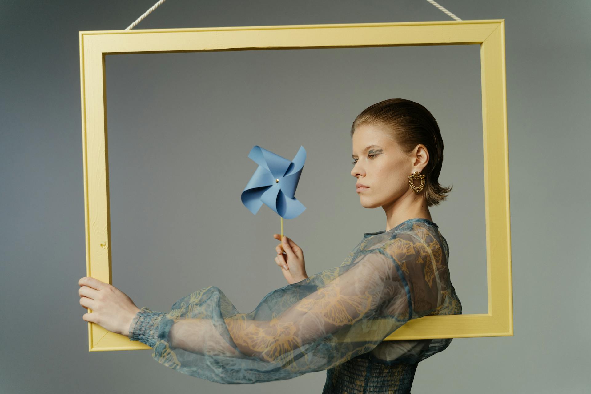 Artistic studio portrait of a model with blue pinwheel in a yellow frame.