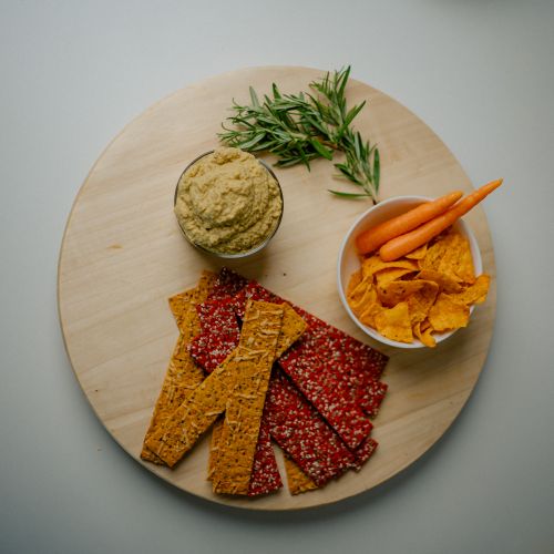 Free Top view of a nutritious snack platter featuring crackers, dip, and vegetables on a wooden tray. Stock Photo
