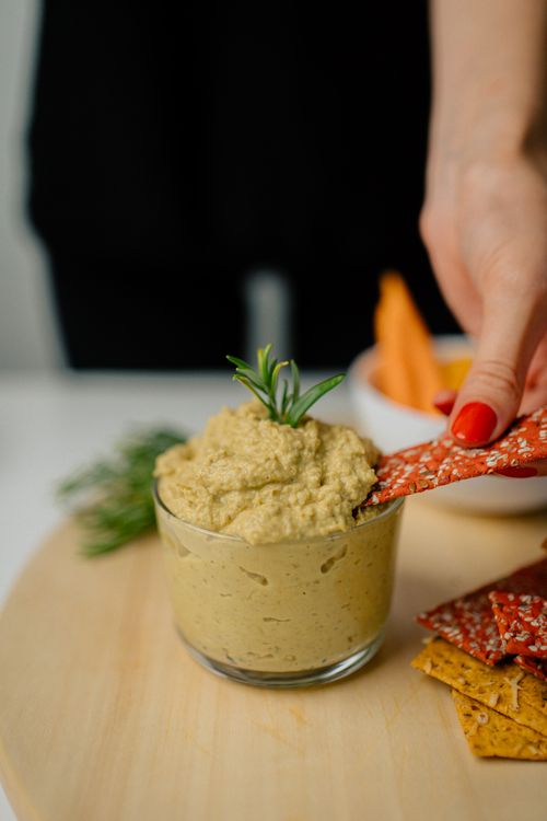 Free A hand dips a cracker into creamy hummus on a wooden tray with garnish. Stock Photo