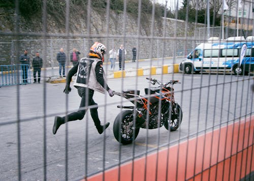 無料 アスファルト道路でオレンジと黒のスポーツバイクを保持している男 写真素材