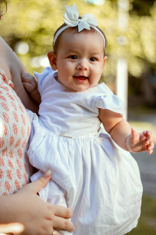 Baby in White Dress Lying on Persons Lap
