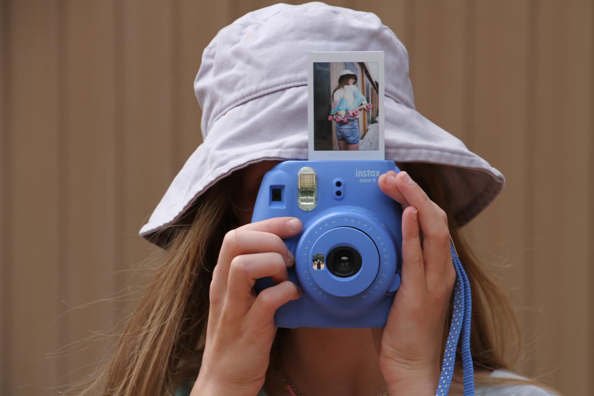 Close-up of a woman wearing a bucket hat using a blue instant camera outdoors.