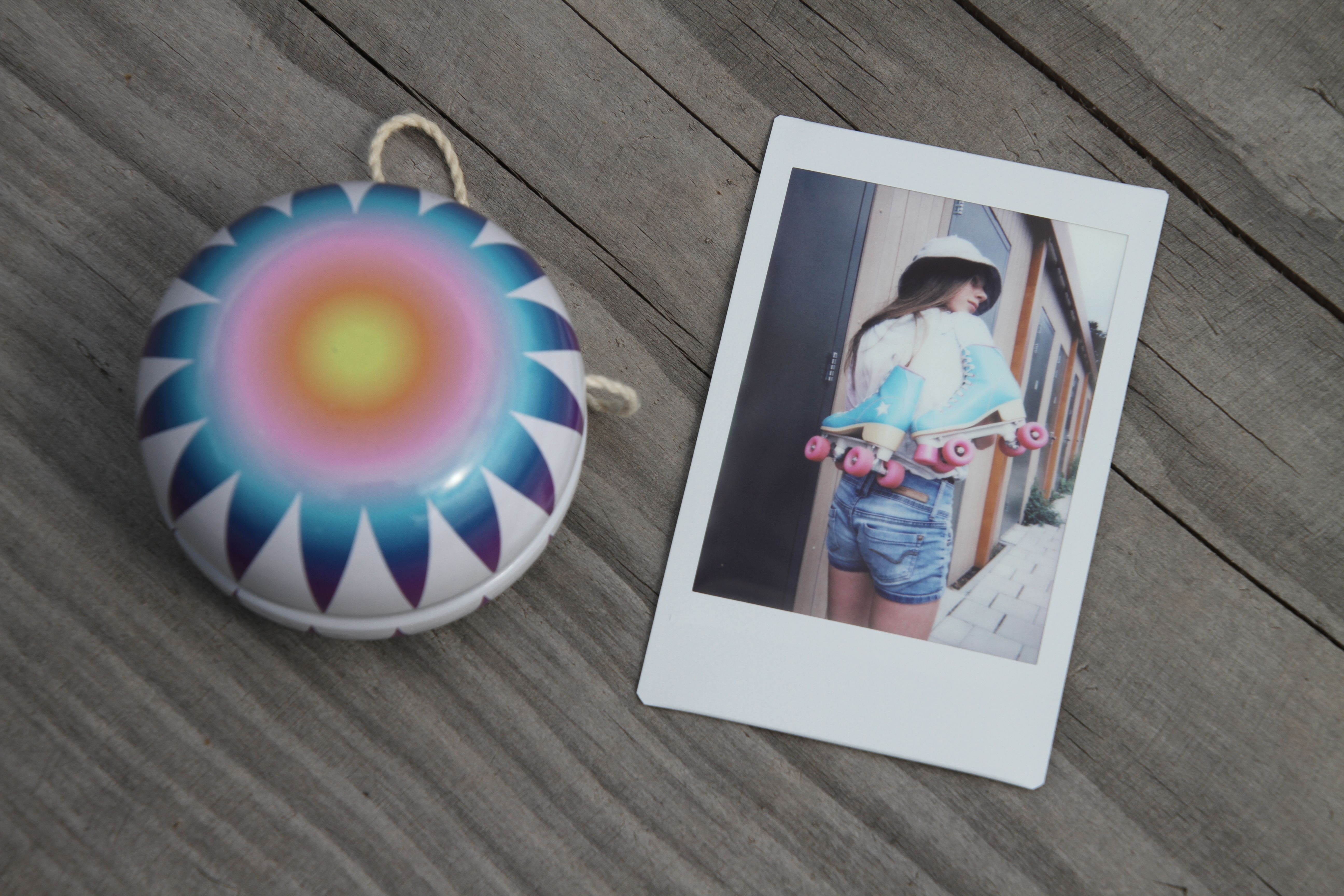 A vibrant yoyo beside a polaroid photo of a woman with roller skates on a wooden background.