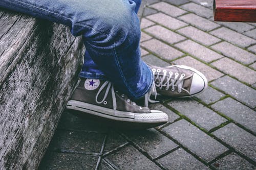 Person, Die Braune Converse All Star High Top Turnschuhe Und Blaue Jeans Trägt, Während Sie Auf Der Bank Sitzt