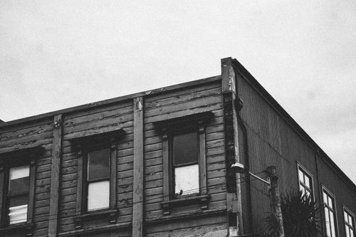 Free Grainy black and white photo of a vintage wooden building's corner with windows. Stock Photo