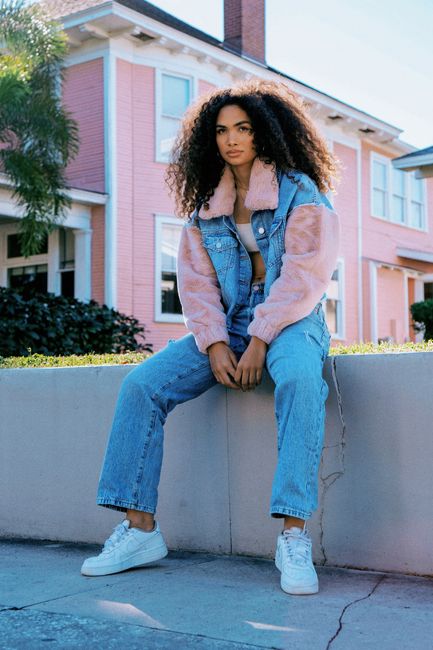 Stylish young woman sitting in denim and fur jacket outdoors.