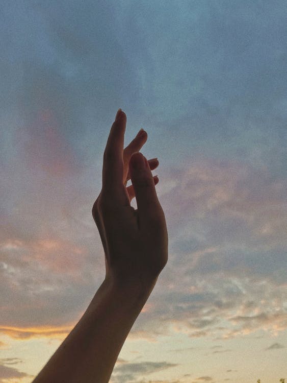 Persons Left Hand With Blue Sky and White Clouds · Free Stock Photo