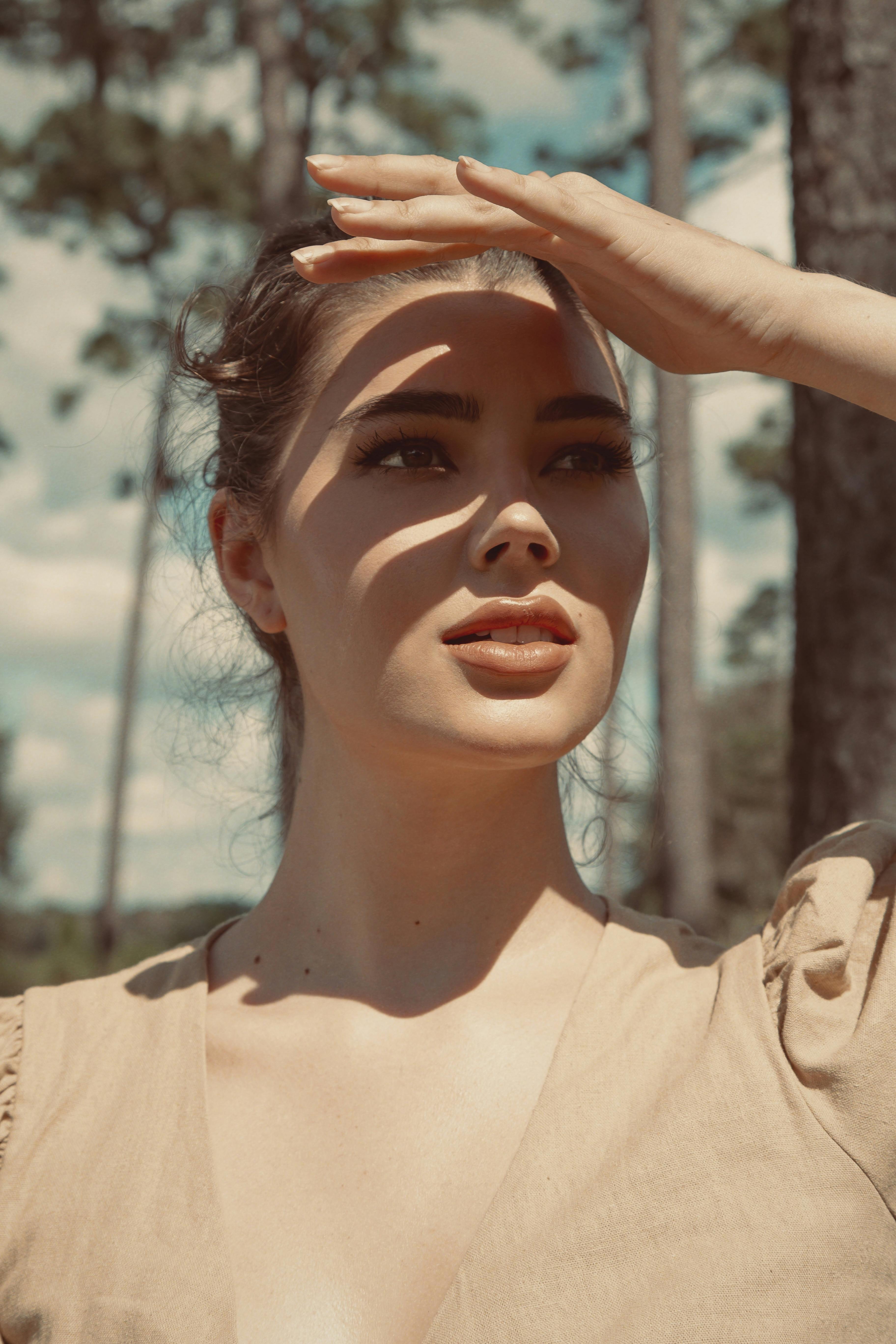 A portrait of a woman outdoors shielding her eyes from the sun, creating a thoughtful pose.