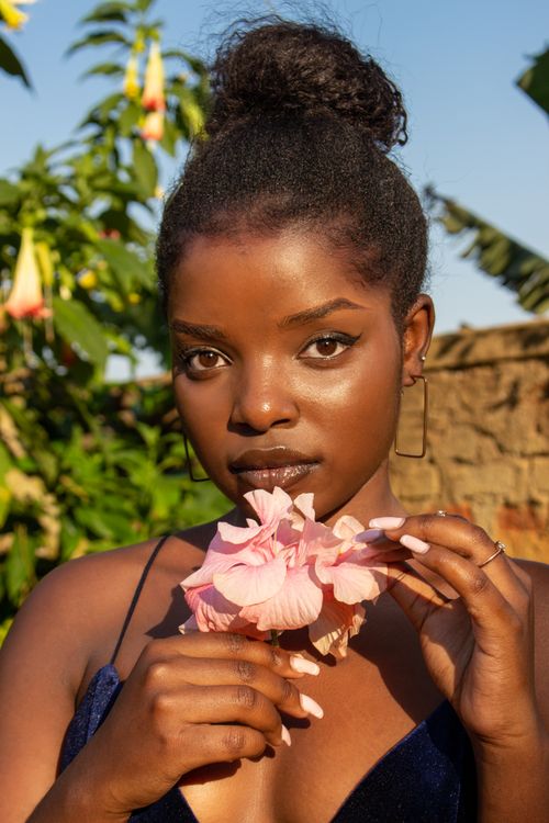Free Elegant portrait of a woman holding delicate pink flowers outdoors in Uganda. Stock Photo