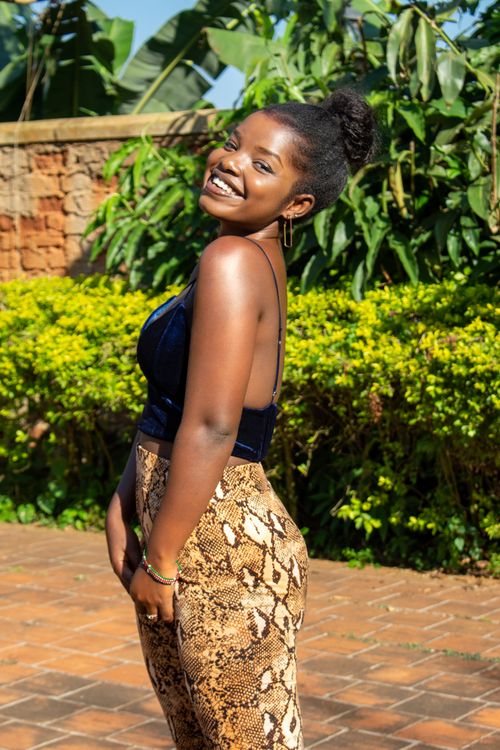 Free Young woman posing outdoors with a vibrant smile and stylish outfit against lush greenery. Stock Photo