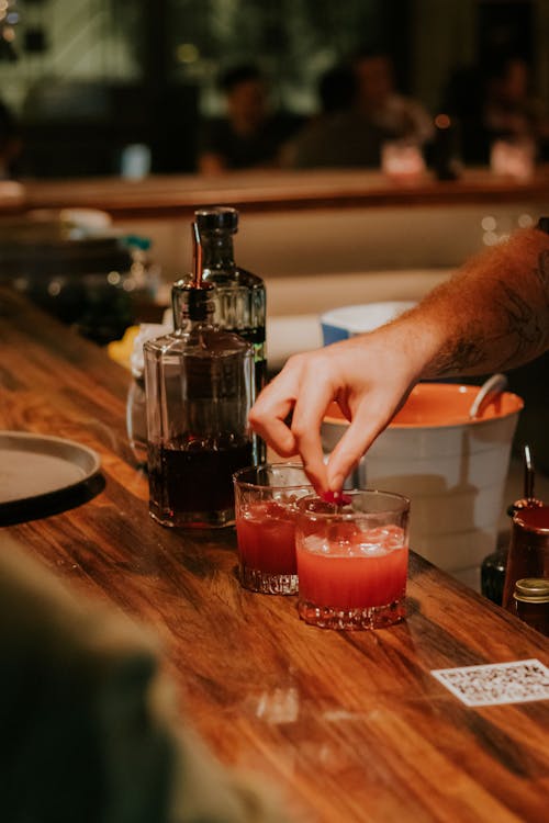 Person Pouring Red Liquid on Clear Glass Cup