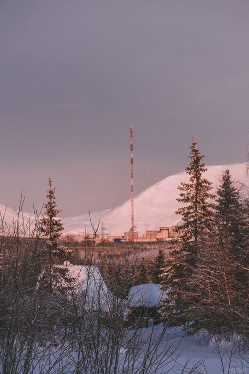 Free A serene winter landscape with a tall tower against snow-covered hills at sunset. Stock Photo