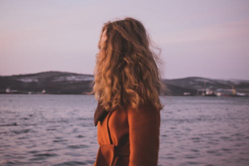 Free Woman in Orange Sleeveless Dress Standing Near Body of Water Stock Photo