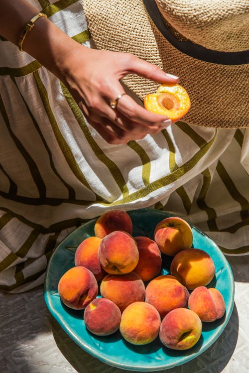 Free A vibrant display of fresh peaches in a bowl with a hand holding a sliced peach in sunlight. Stock Photo