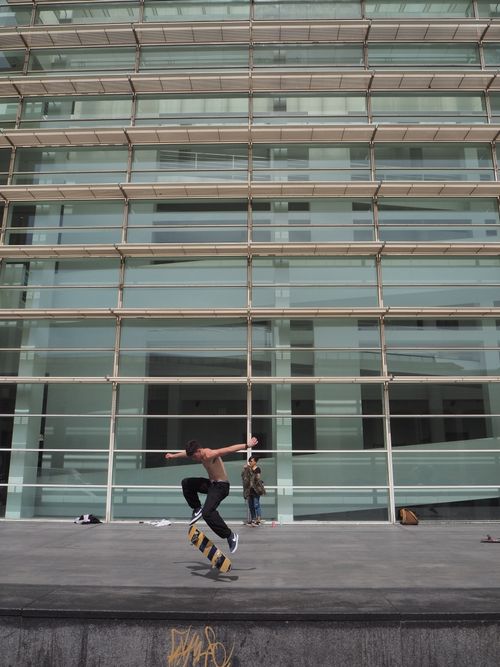 Free Skateboarder performing a trick in front of a modern building facade in Barcelona. Captures urban lifestyle. Stock Photo