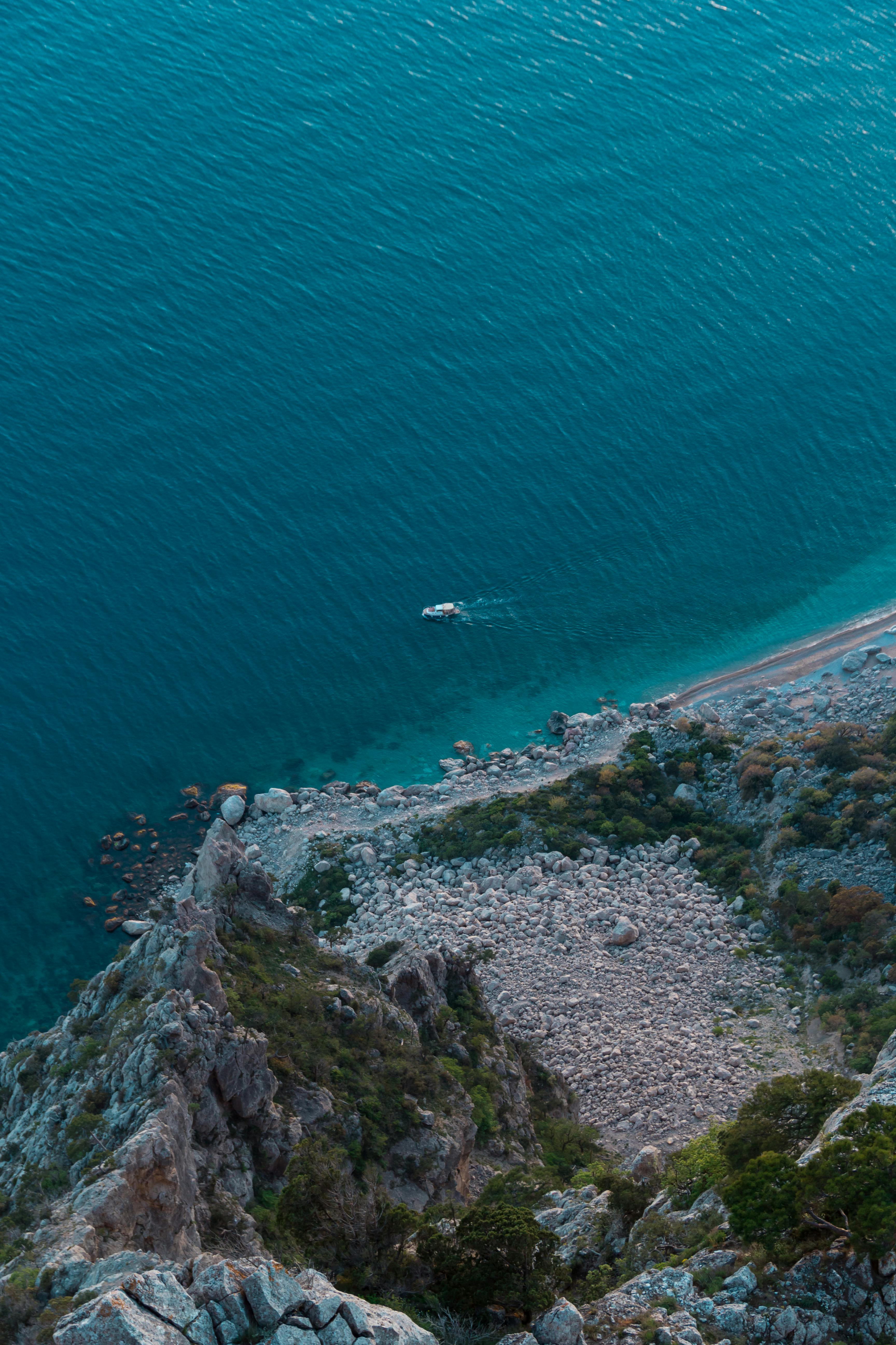 Free Stunning aerial photo of a boat on a clear blue sea near a rocky coastline. Stock Photo