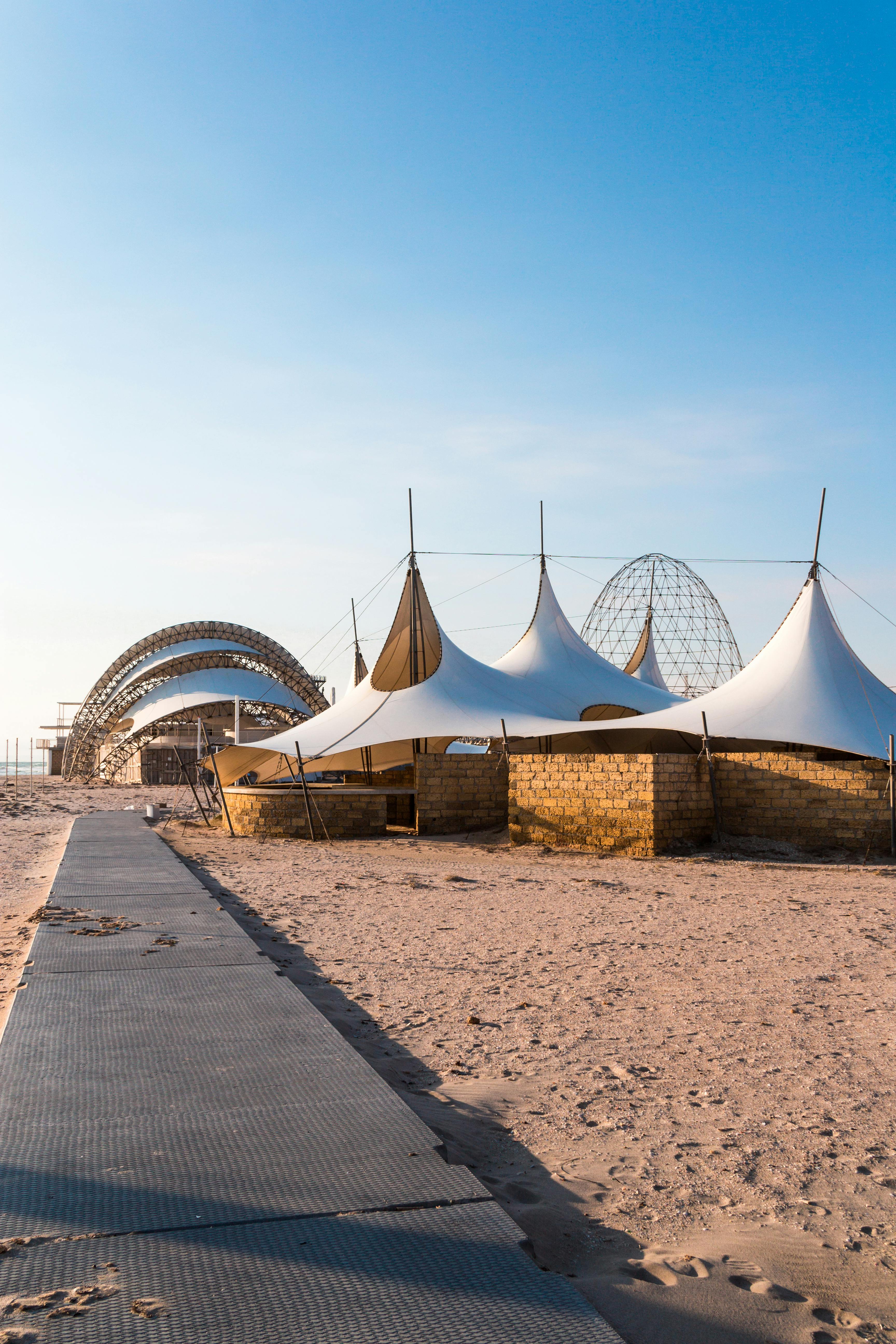 Stylish tent and structure setup on a sunny beach with a clear blue sky.