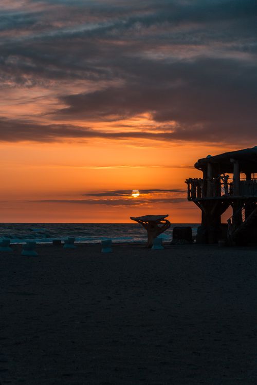 Free Stunning sunset view over ocean with silhouetted beach hut capturing serene beauty. Stock Photo