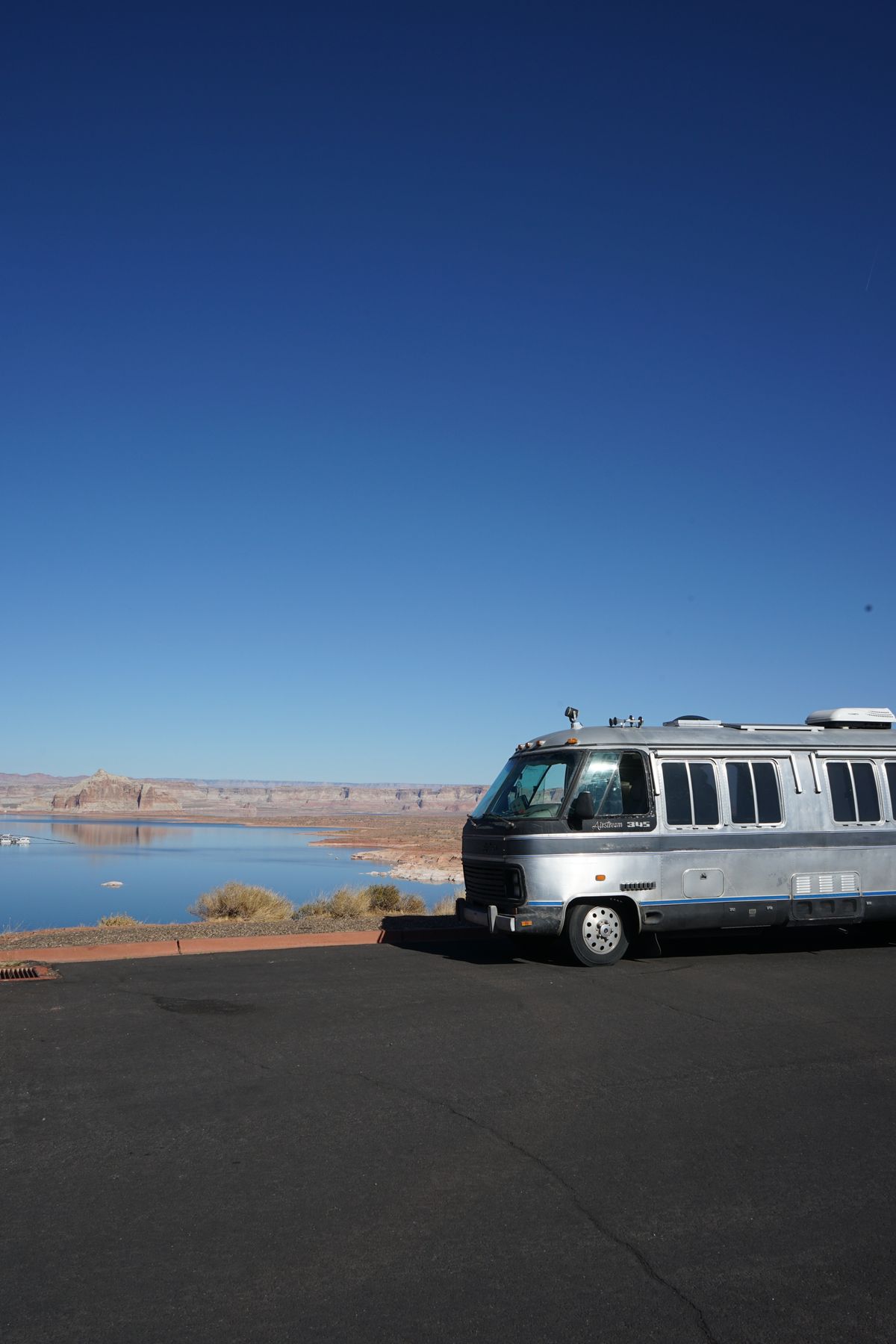 A silver travel trailer parked beside a lake under a clear blue sky in Arizona