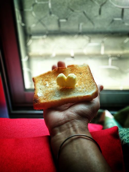 Free A slice of toasted bread with heart-shaped butter on a hand near a window. Stock Photo