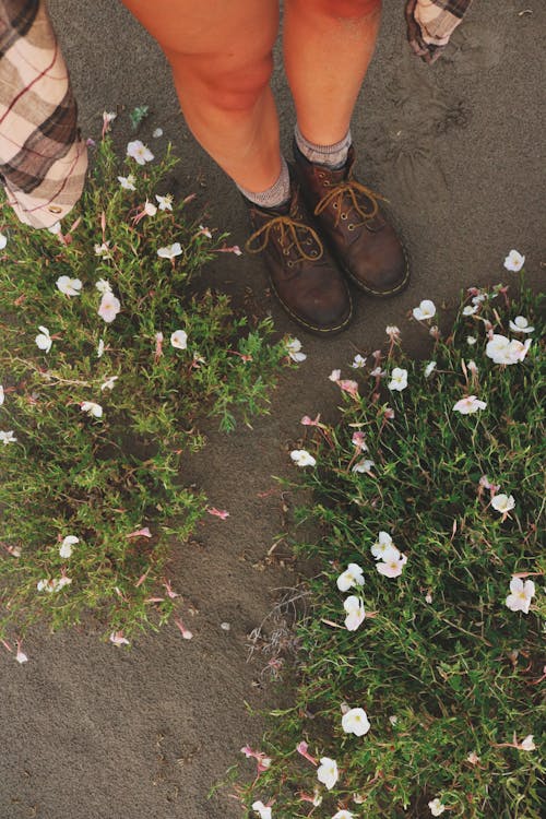 Person in Brown Ankle Boots Standing next to White Flowers