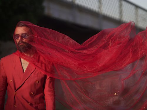 Man on a Fashion Shoot Wearing a Red Suit and Sheer Red Fabric Over His Head 