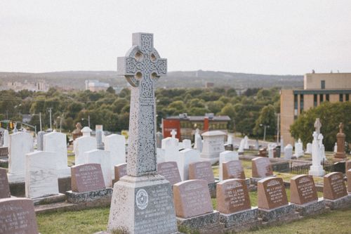 Free Peaceful cemetery view showcasing a prominent Celtic cross tombstone surrounded by gravestones. Stock Photo