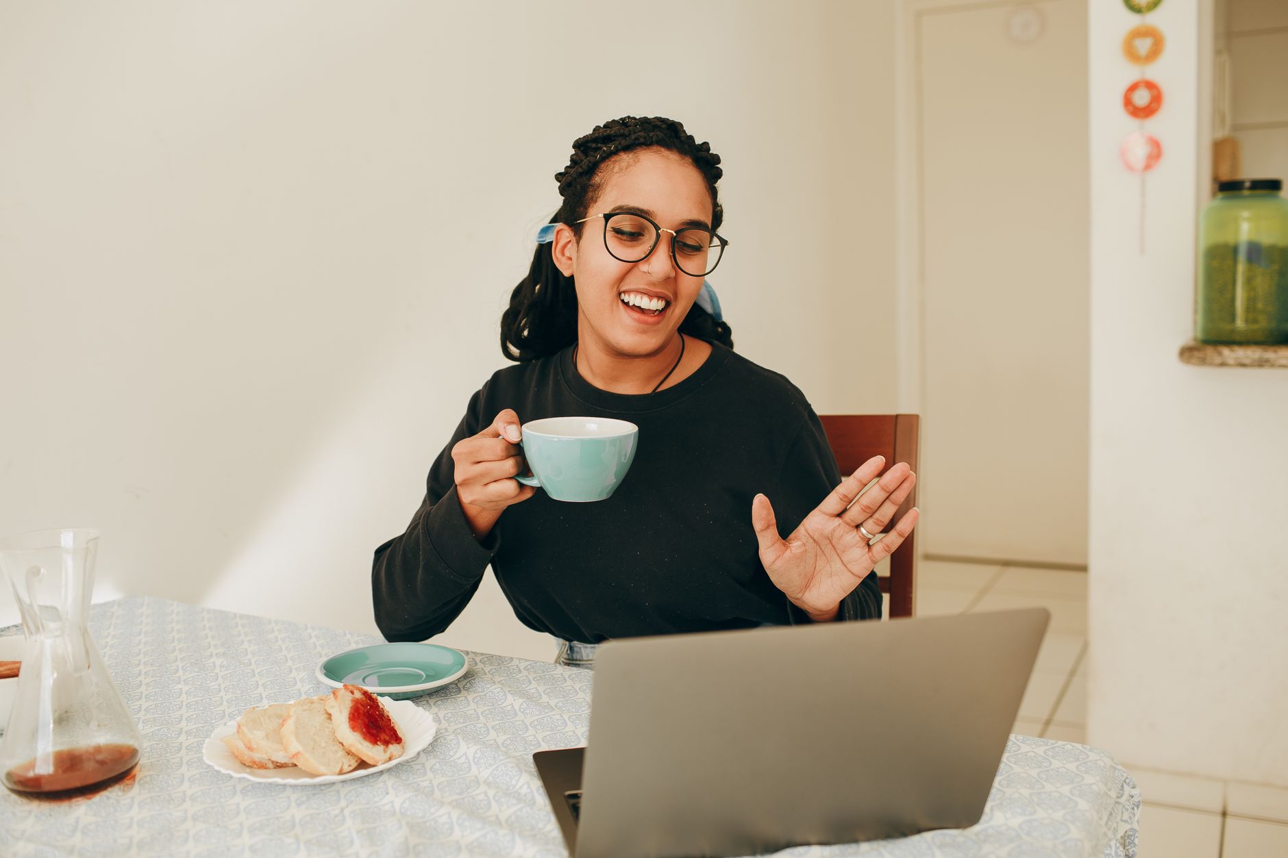 Jeune femme à lunettes souriante, tasse à la main, lors d'un appel vidéo sur un ordinateur portable