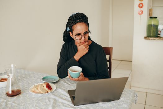 A woman sips coffee while intently focused on her laptop, indoors.