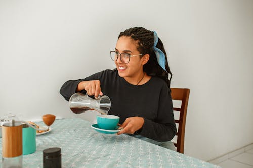 A Woman in Black Sweater Pouring Coffee on a Ceramic Cup with Saucer