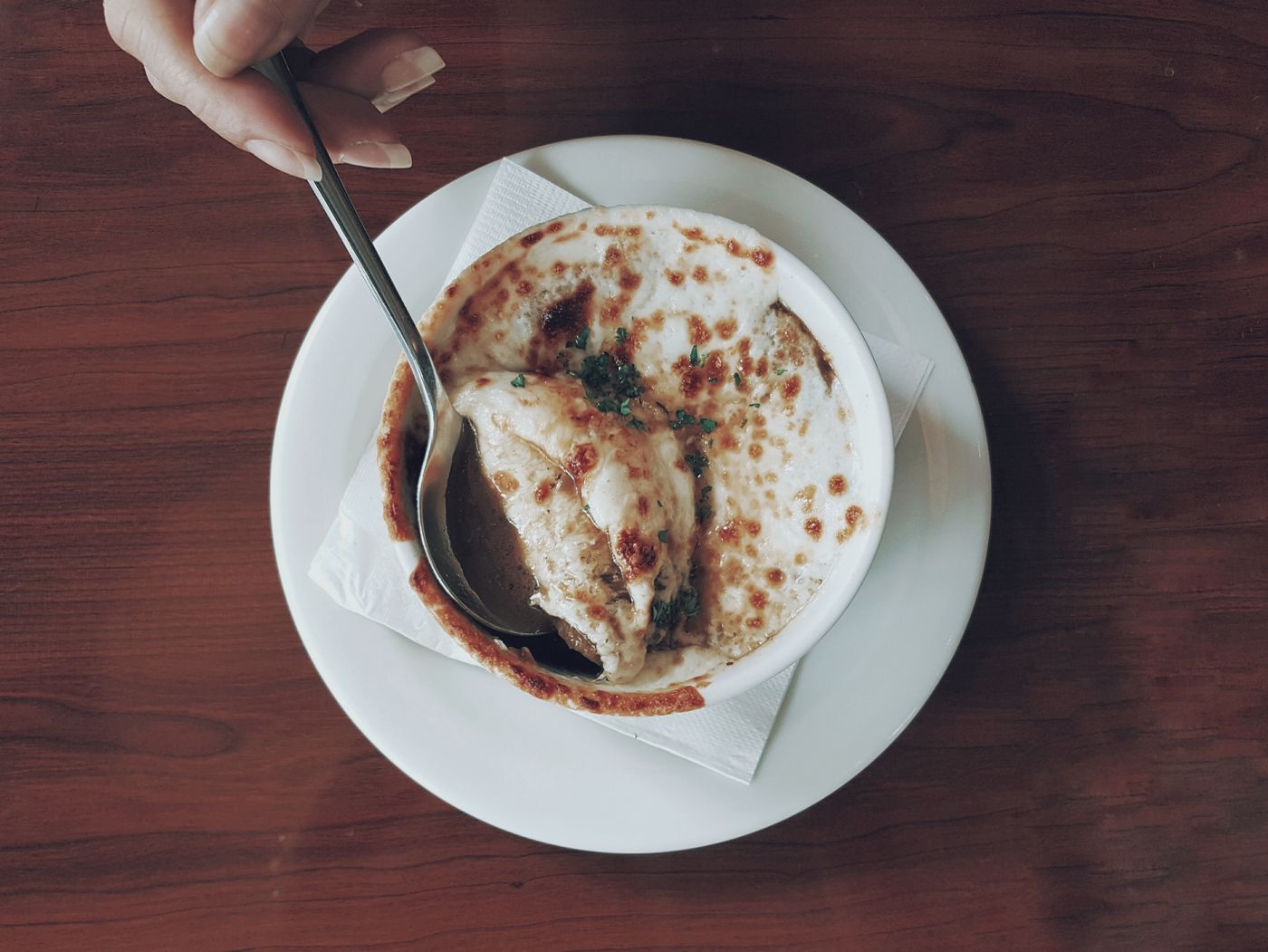 Top view of gourmet French onion soup with melted cheese in a ceramic bowl, served with a spoon.