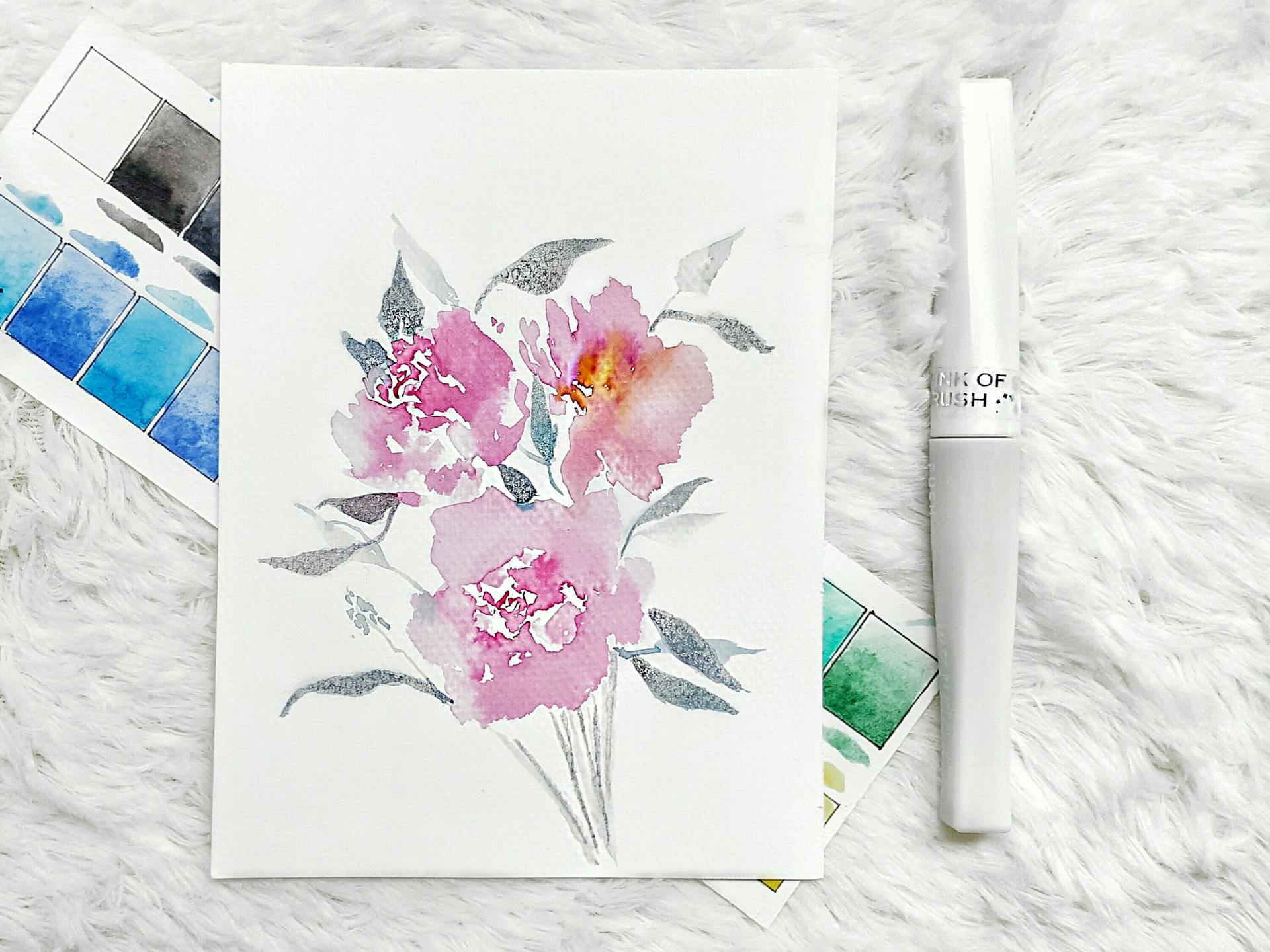 Artistic watercolor painting of pink flowers with a palette and brush on soft fabric.