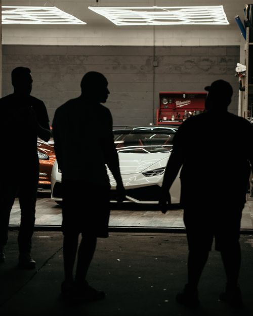 Free Dramatic silhouettes of people in front of a luxury supercar in a garage setting. Stock Photo