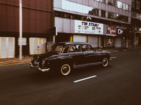 Classic black Mercedes Benz driving on empty urban street.