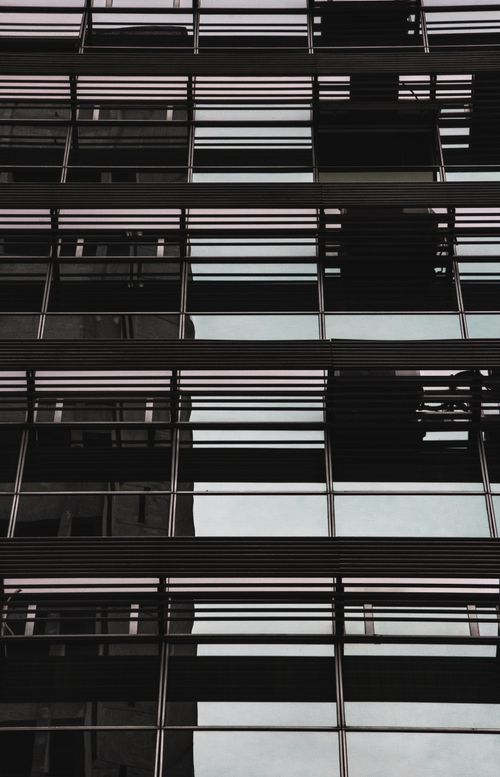 Free Close-up of a modern glass facade reflecting an urban cityscape with symmetrical lines. Stock Photo