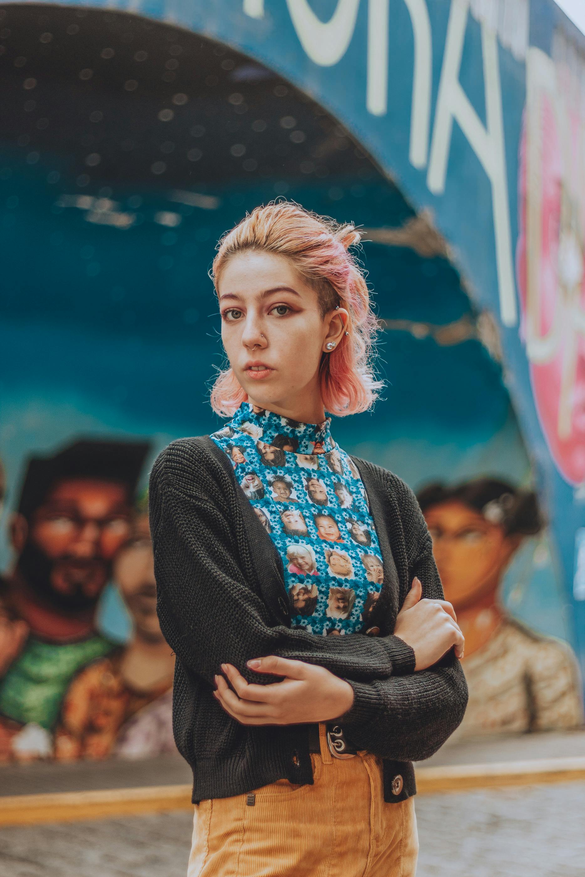 Portrait of a fashionable woman with pink hair posing in front of a vibrant urban graffiti wall.