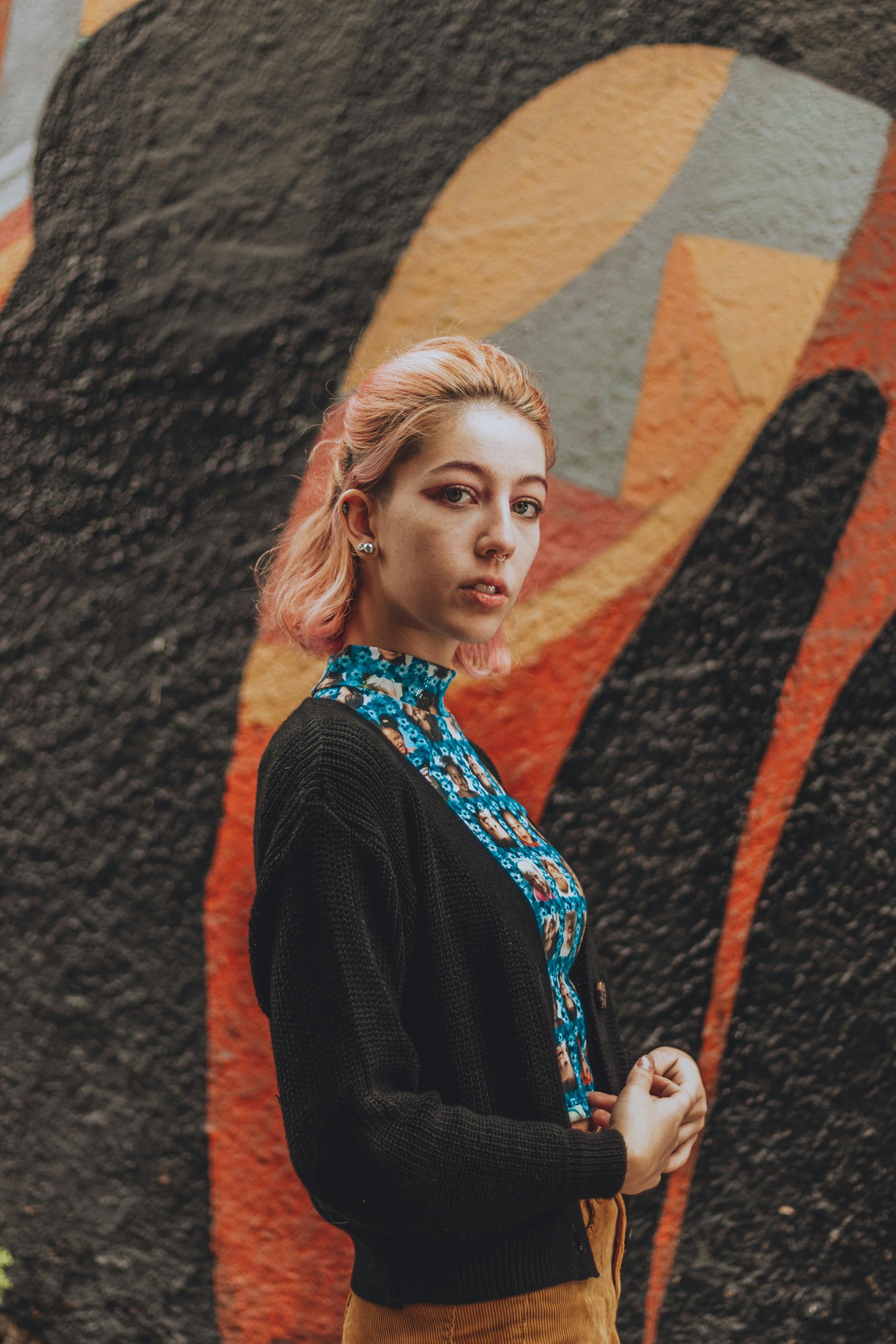 Confident woman with colored hair poses outdoors against vibrant mural art.