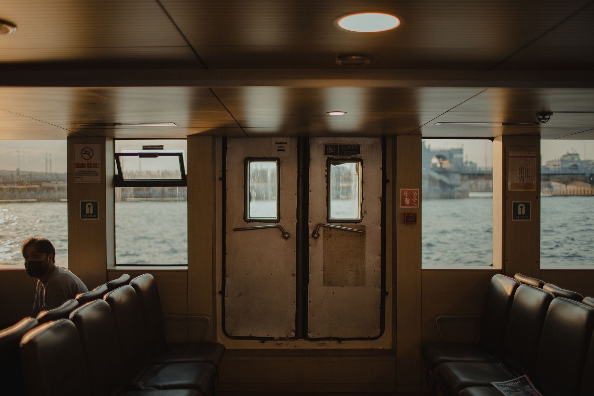 Cozy passenger boat interior with sunset view in İstanbul, showcasing tranquil water and cityscape.