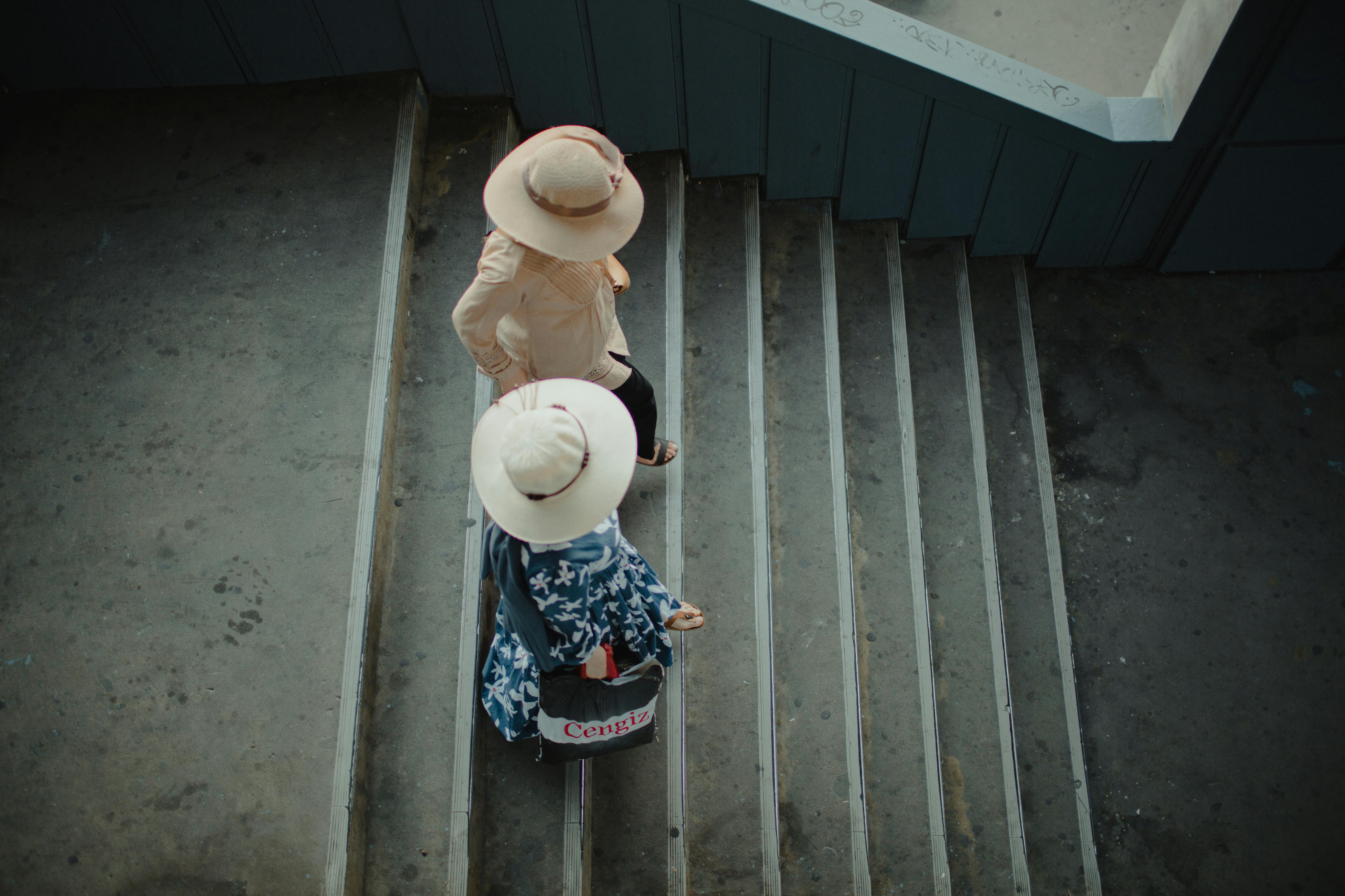 Two women wearing hats walking down stairs in Istanbul, Türkiye, captured from above.