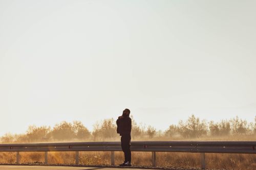 Free Silhouette of a man standing on a highway with a bright sky and foliage backdrop. Stock Photo