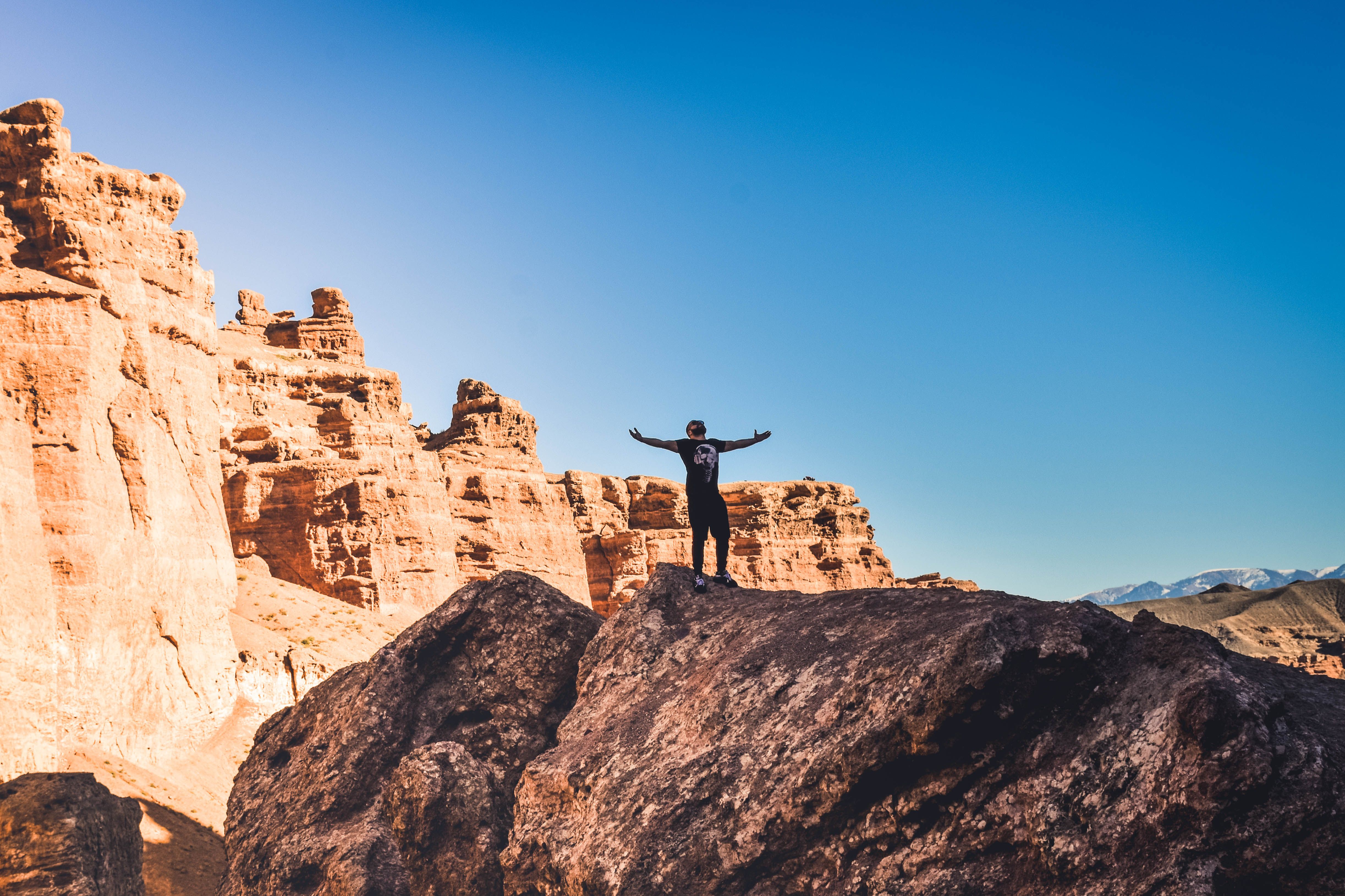 A hiker stands triumphantly on a boulder amidst red rock formations under a clear blue sky.