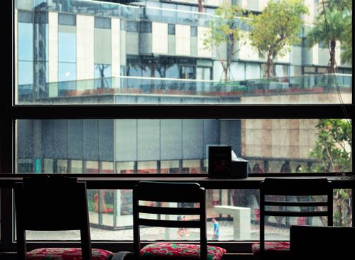 Free Minimalist cafe interior featuring empty wooden chairs and large glass window showcasing urban cityscape. Stock Photo
