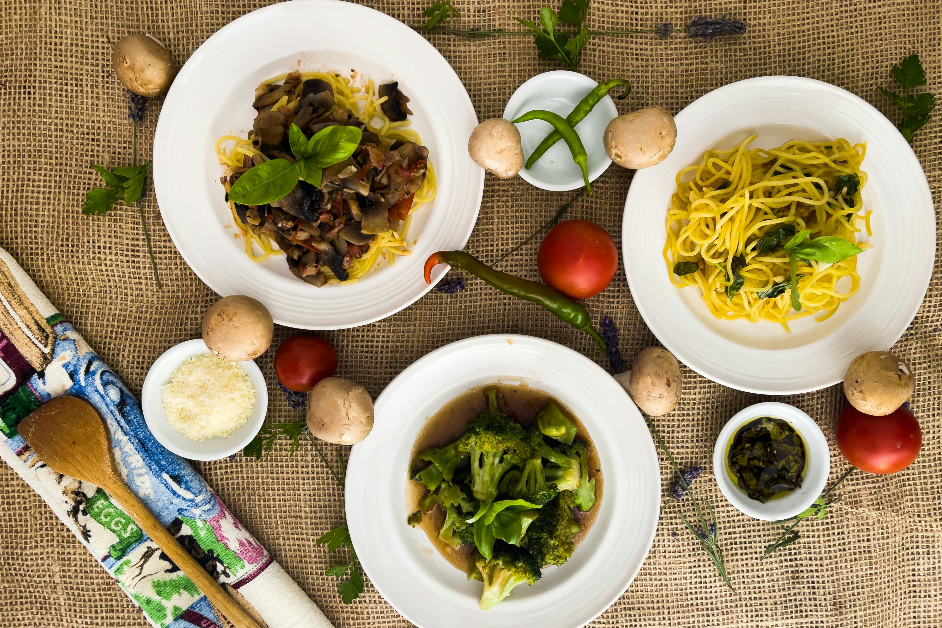 Top view of assorted pasta dishes with fresh ingredients on a rustic table setting.