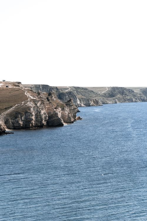Free Breathtaking view of rugged cliffs meeting the expansive blue sea under a white sky. Stock Photo