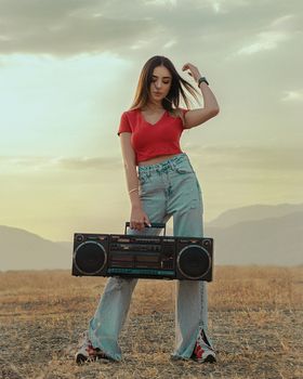 Trendy young woman holding a vintage boombox in a serene outdoor setting.