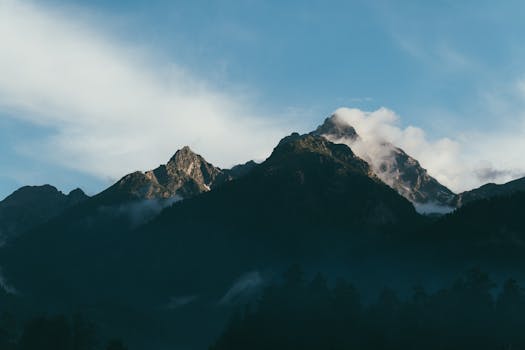 Scenic mountain peaks with clouds under a clear blue sky.