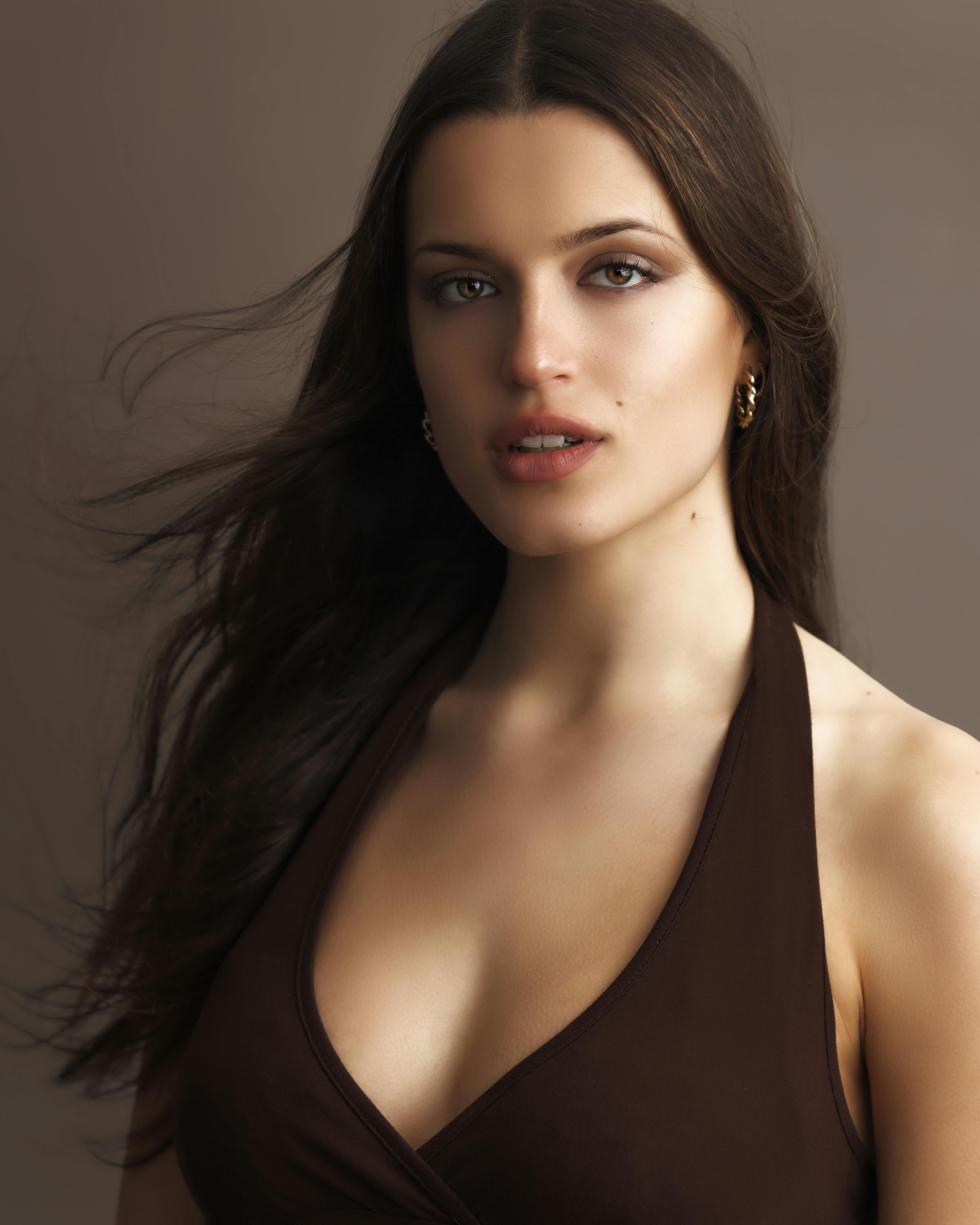 Stunning portrait of a young woman with long hair wearing a brown top in a studio setting.