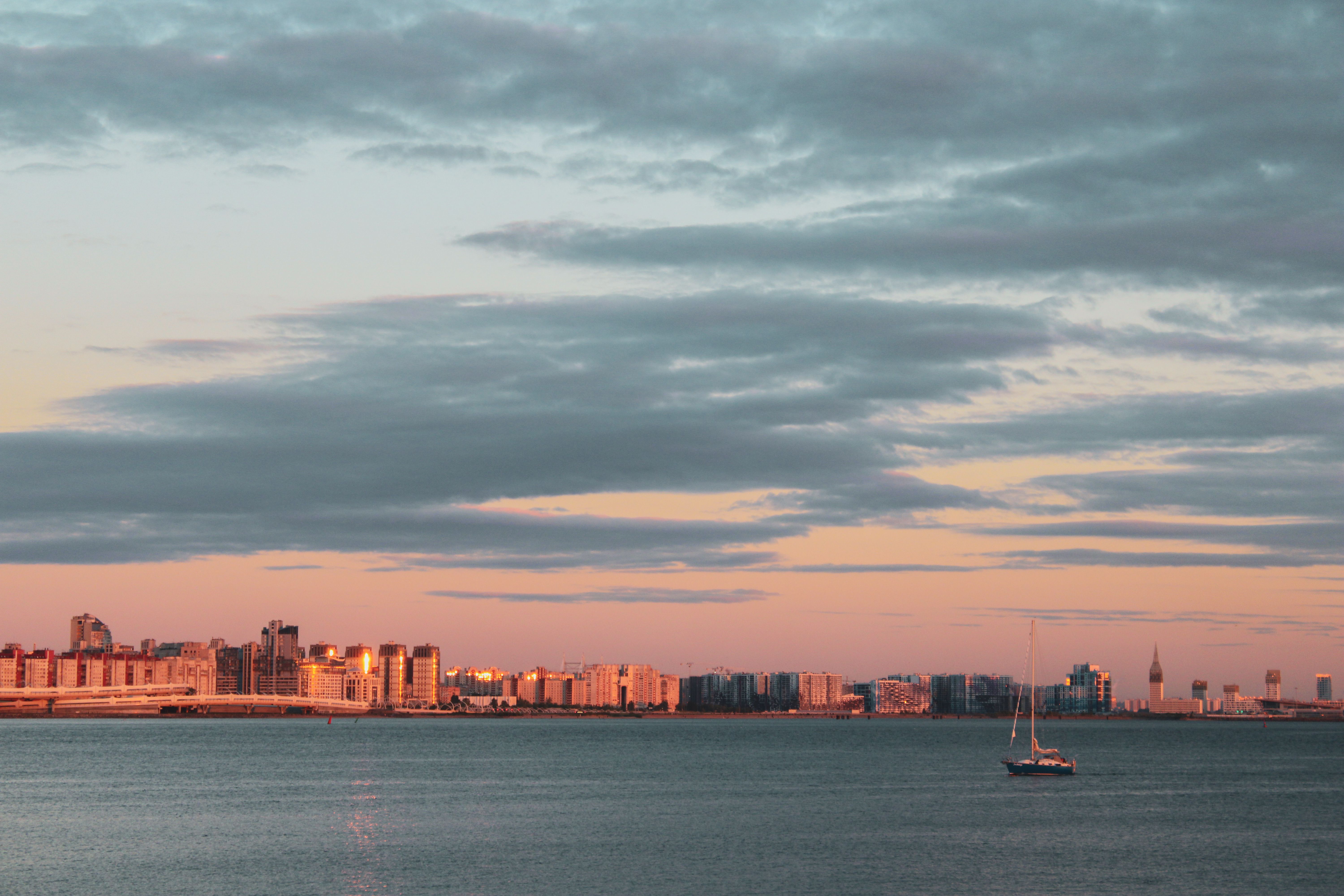 Serene view of St. Petersburg skyline with dramatic clouds and a sailboat at sunset.