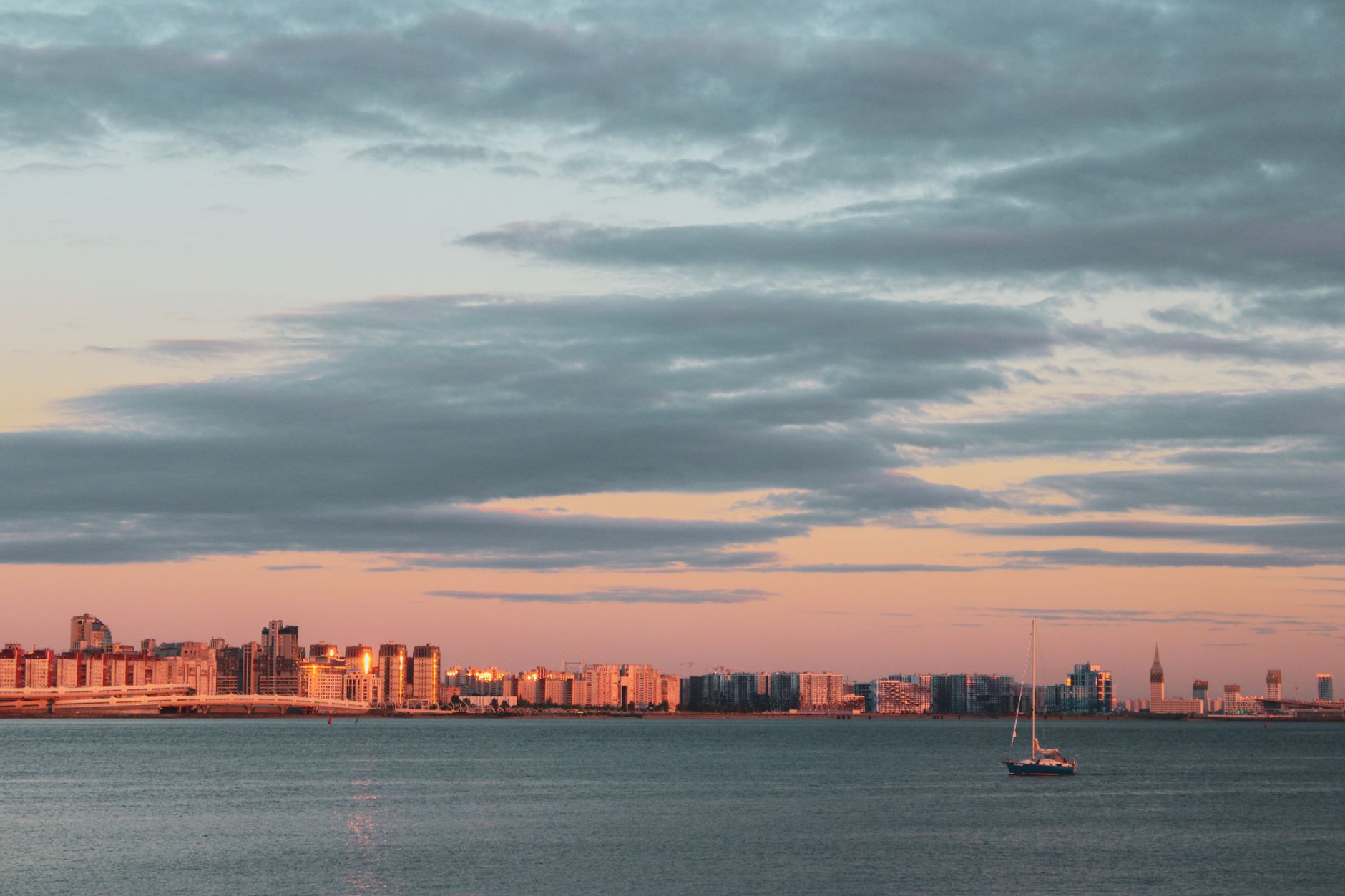 Serene view of St. Petersburg skyline with dramatic clouds and a sailboat at sunset.